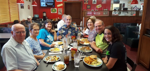 A group of eight people enjoying a meal together at a restaurant, with plates of food and drinks on the table.