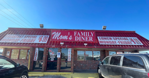 Exterior of Mom's Family Diner with a red roof, signs for breakfast and lunch specials, and clear blue sky.