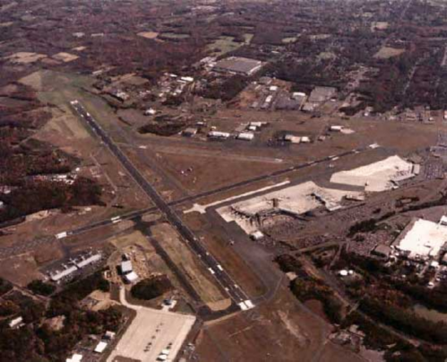 Aerial view of an airport with runways, surrounding buildings, and parking areas in a rural landscape.