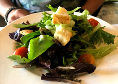 A fresh salad with mixed greens, cherry tomatoes, croutons, and diced cucumber on a white plate.