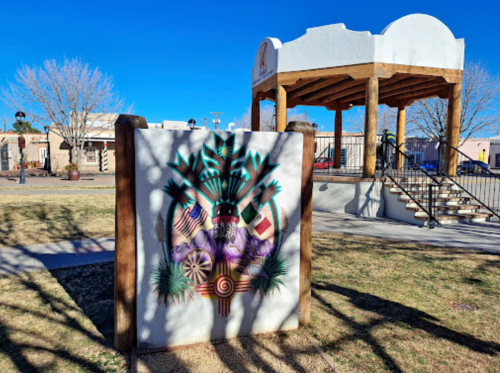 A colorful mural featuring flags and symbols, next to a gazebo in a park with clear blue skies.