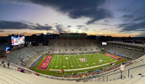 A panoramic view of a nearly empty stadium at sunset, featuring the field marked with "WILDCATS" and surrounding mountains.