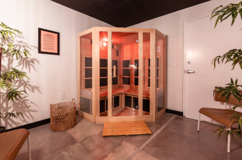 A wooden infrared sauna in a serene room with plants and seating, featuring warm lighting and a welcoming atmosphere.
