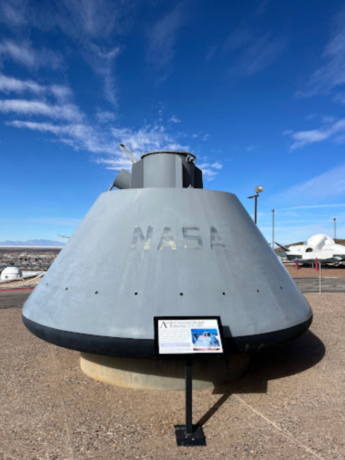 NASA spacecraft on display outdoors, with a clear blue sky and informational sign nearby.