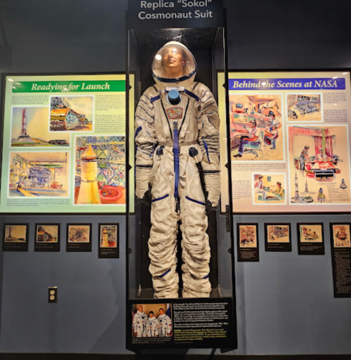 A replica "Sokol" cosmonaut suit displayed in a museum, with informational panels about NASA and space missions.