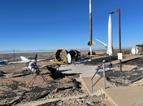 Outdoor display of various missiles and rockets against a clear blue sky, with a view of the surrounding landscape.