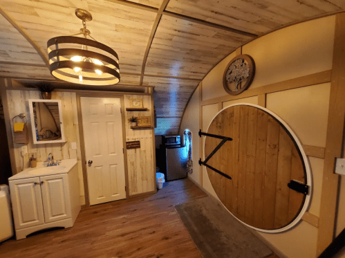 Interior of a cozy room featuring a round folding table, a sink, a door, and a small kitchenette area.