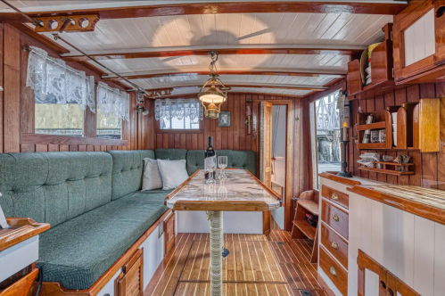 Cozy interior of a boat featuring a green cushioned seating area, wooden accents, and a dining table with a bottle and glasses.