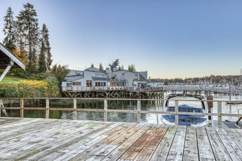 A waterfront view of a dockside building with boats and trees in the background under a clear sky.