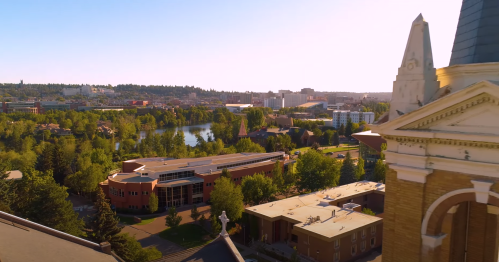 Aerial view of a city with green trees, buildings, and a river under a clear sky.