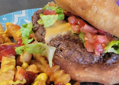A close-up of a juicy burger with lettuce, tomato, and cheese, served with crinkle-cut fries and condiments on the side.