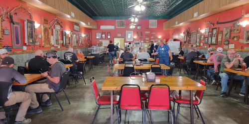 A bustling restaurant interior with wooden tables, red chairs, and patrons enjoying meals amidst rustic decor.