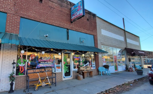 A storefront decorated for the holidays, featuring lights and festive displays, with a blue awning and sidewalk seating.