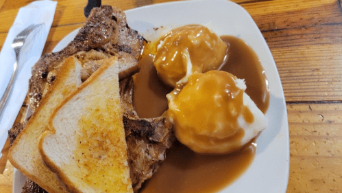 A plate with grilled meat, two mashed potato servings topped with gravy, and slices of toasted bread.