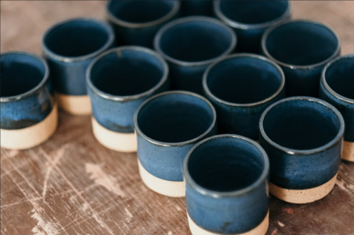 A collection of blue ceramic cups with beige bases arranged on a wooden surface.