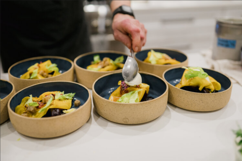 A chef adds a garnish to bowls of colorful, plated food on a kitchen counter.