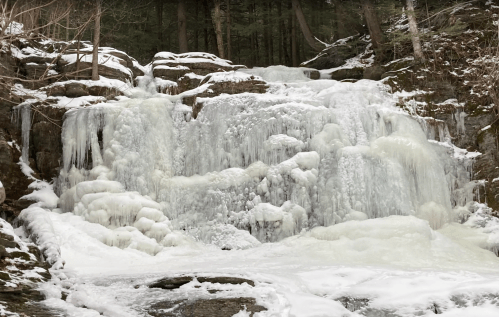 A frozen waterfall surrounded by snow-covered rocks and trees, creating a serene winter landscape.