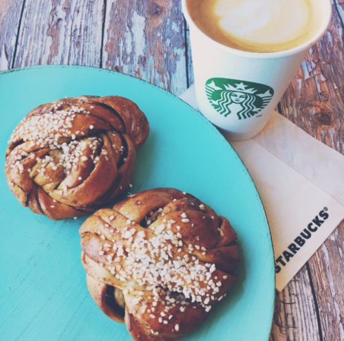 Two cinnamon buns with sugar on a turquoise plate, next to a Starbucks coffee cup and a napkin.