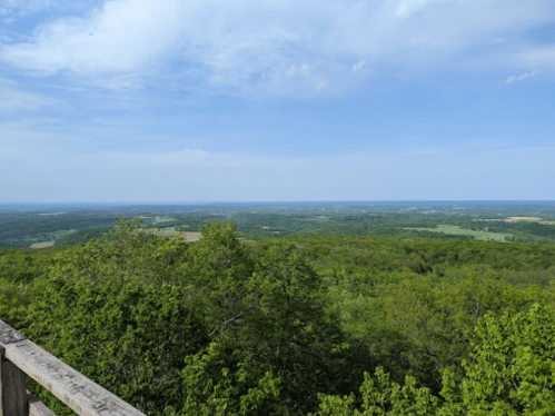 A panoramic view of lush green hills and valleys under a blue sky with scattered clouds.