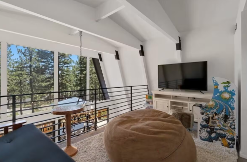 Bright, modern living space with large windows, a TV, bean bag, and a unique art piece, surrounded by trees.