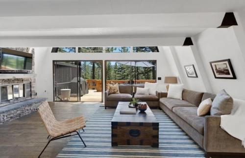 Modern living room with a cozy sofa, wooden accents, and large windows overlooking a forested deck.