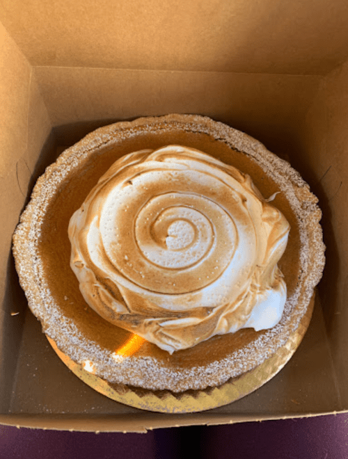 A beautifully swirled meringue topping on a golden pie crust, inside a cardboard box.