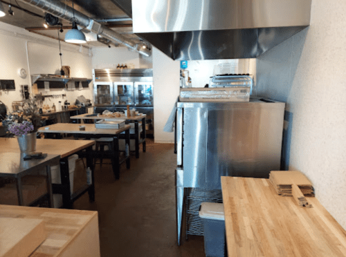 A modern kitchen with stainless steel appliances, wooden tables, and a clean, organized workspace.