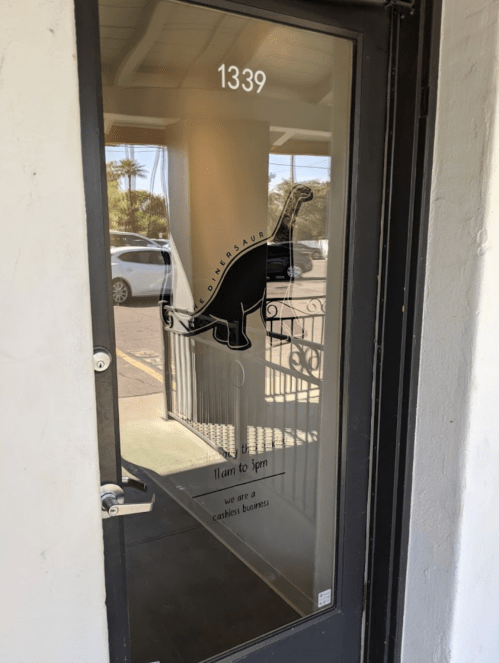 A glass door with a dinosaur logo and text reading "11am to 5pm, we are a cashless business" at 1339.