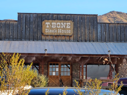 Sign for T-Bone Steak House on a rustic wooden building with a mountain backdrop.