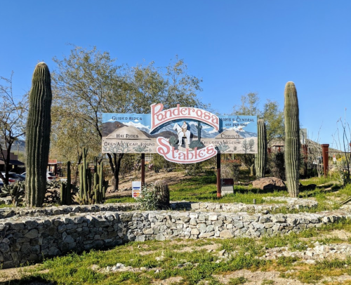 Sign for Ponderosa Stables with cacti and a clear blue sky in the background.