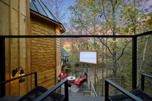 View from a balcony overlooking a wooded area at sunset, featuring a cozy outdoor seating arrangement.