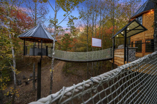 A treehouse with a bridge connecting two towers, surrounded by colorful autumn foliage.