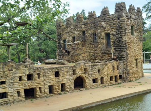 A stone castle-like structure in a zoo, surrounded by greenery and a small water feature.