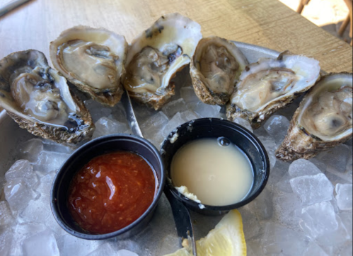 A plate of fresh oysters on ice, served with cocktail sauce, mignonette, and a lemon wedge.