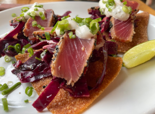 Three crispy taco shells topped with seared tuna, red cabbage, and green onions, served with a lime wedge.