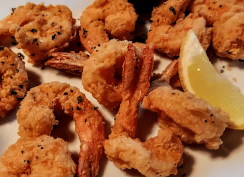 A plate of crispy fried shrimp garnished with parsley and a lemon wedge.
