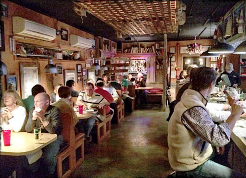 A cozy restaurant interior with diners at tables, warm lighting, and walls adorned with pictures and decor.