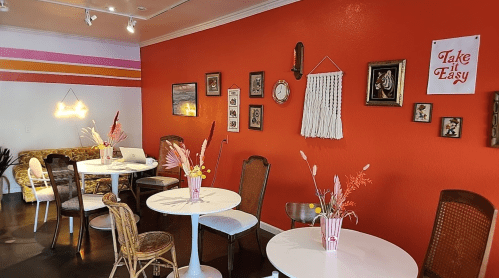 Cozy café interior with orange walls, white tables, vintage decor, and floral centerpieces. Relaxed atmosphere.