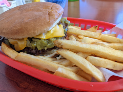 A cheeseburger with pickles and melted cheese served with a side of golden French fries in a red basket.