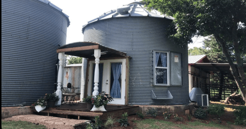 Two metal silos converted into a cozy home, featuring a wooden porch and decorative plants.