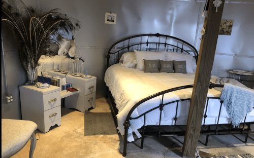 Cozy bedroom with a metal bed frame, white bedding, a mirror, and decorative elements in a stylish, modern design.