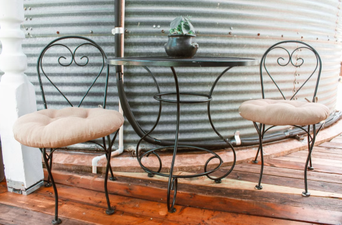 A small round table with two heart-shaped chairs, set on a wooden deck beside a corrugated metal wall.