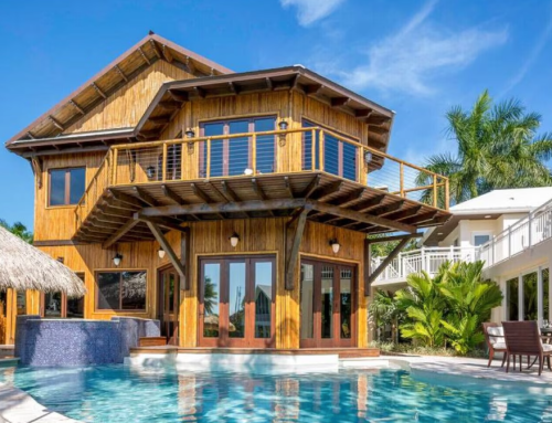 A modern wooden house with a pool, surrounded by palm trees and a clear blue sky.