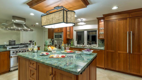 A modern kitchen with wooden cabinets, a large island, and a spread of food and drinks on the countertop.