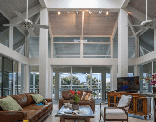Spacious living room with high ceilings, large windows, a brown leather sofa, and tropical decor.