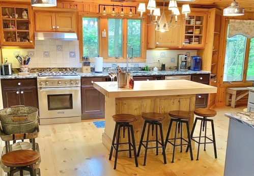 A cozy kitchen with wooden cabinets, a large island, bar stools, and natural light from windows.