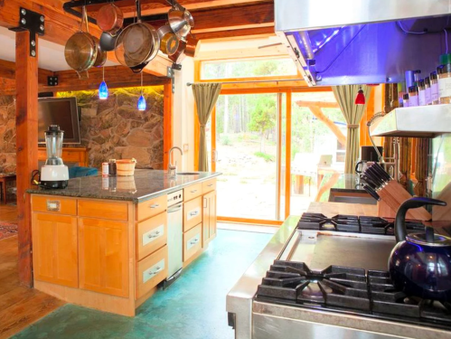 Bright kitchen with wooden cabinets, a large island, stainless steel appliances, and a view of the outdoors through glass doors.