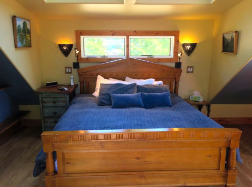 Cozy bedroom featuring a wooden bed with blue bedding, two windows, and warm yellow walls.