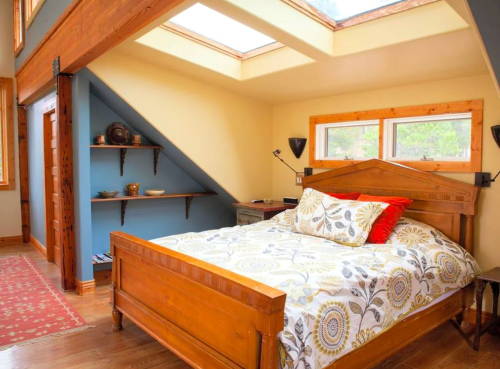 Cozy bedroom with a wooden bed, colorful bedding, skylights, and a warm, inviting atmosphere.