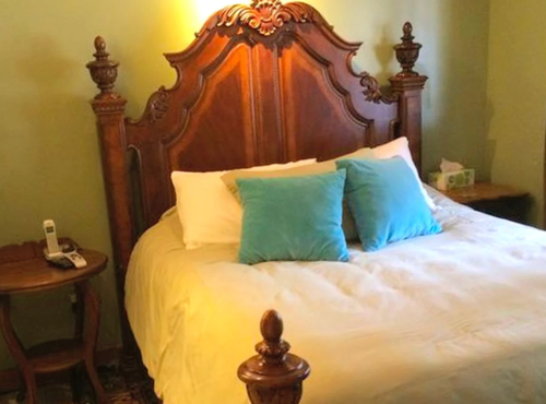 A cozy bedroom featuring a wooden bed with decorative headboard and two blue pillows, alongside a small bedside table.